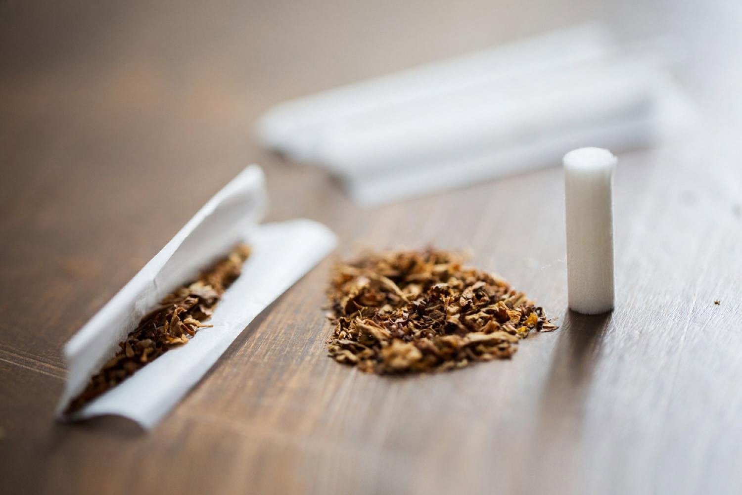 Loose tobacco, rolling paper and a filter arranged on a wooden surface